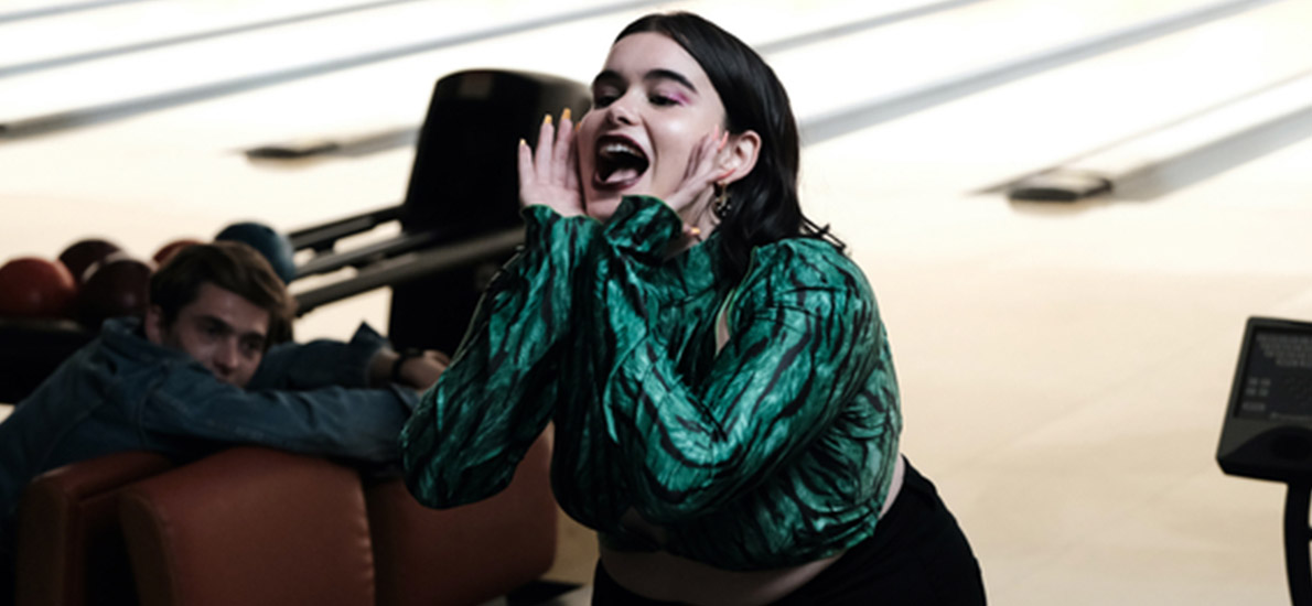 Barbie Ferreira from Euphoria wearing a shimmery green top, in a bowling alley, with her hands cupped around her face, yelling something