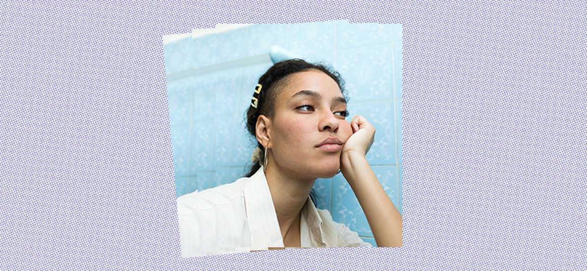 Portrait of a young Black woman without makeup looking bored with a hand in her face in a blue bathroom.