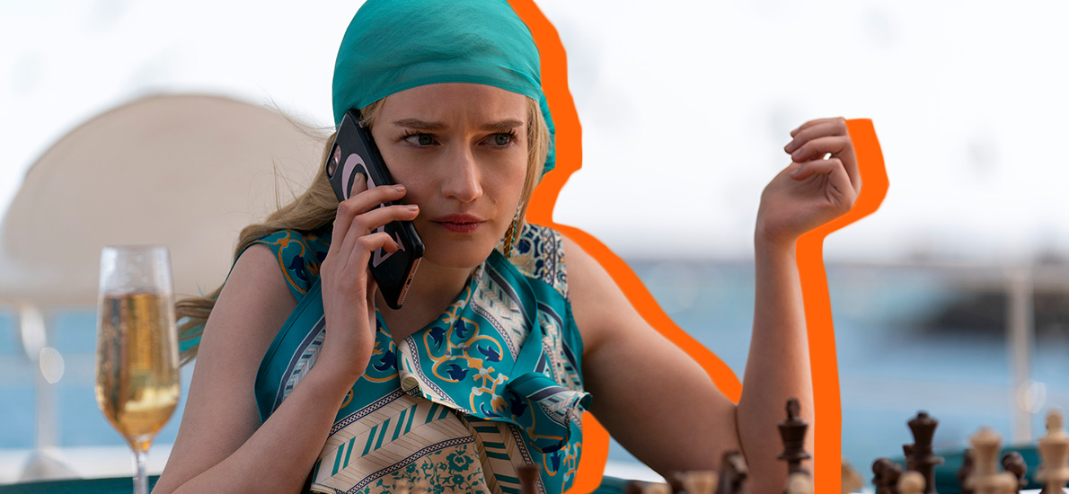Julia Garner as Anna Delvey wears a turquoise head scarf, holding her phone to her ear, looking perplexed