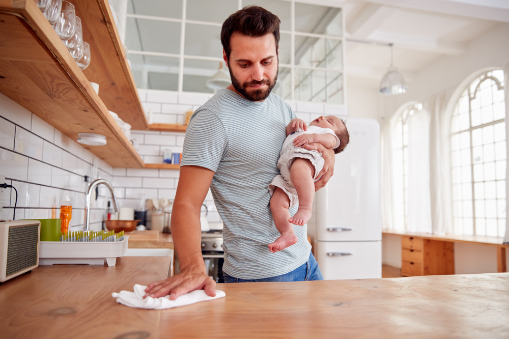 Multi-tasking,Father,Holds,Sleeping,Baby,Son,And,Cleans,In,Kitchen