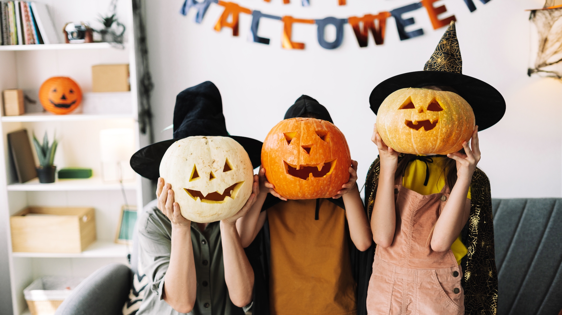 Family in witch hats and carved pumpkins, having fun at home for halloween. Smiling, crafting, and decorating together, creating special memories